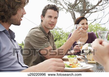 Stock Photograph - Friends eating, drinking and socialising at table outdoors. Fotosearch