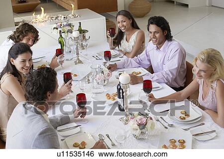 Friends sitting together at Dinner Party, drinking and socialising, elevated view View Large Photo Image Stock Photograph - Friends sitting together at Dinner Party, drinking and socialising, elevated view. Fotosearch