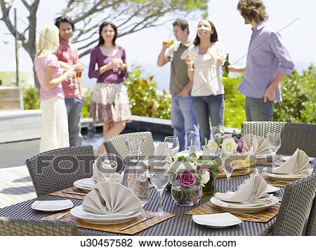 Stock Image - Friends standing outside, drinking, near a set table . Fotosearch