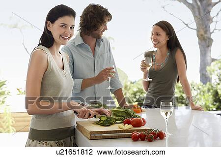 Stock Image - Friends talking, drinking wine, preparing food at a dinner party outside. Fotosearch