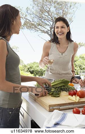 Stock Photo - Friends talking, drinking wine, preparing food at a dinner party outside. Fotosearch