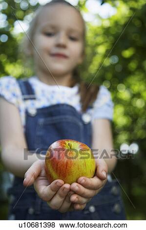 Stock Photo - Girl (5-6) holding apple, focus on apple. Fotosearch