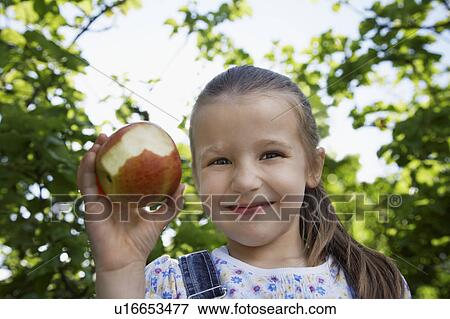 Girl (5-6) holding half-eaten apple, outdoors, portrait View Large Photo Image Stock Photo - Girl (5-6) holding half-eaten apple, outdoors, portrait. Fotosearch