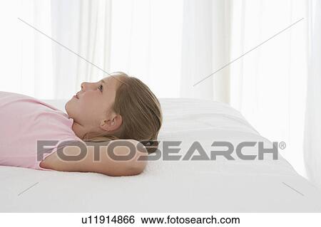 Stock Photograph - Girl lying on bed, profile, half-length. Fotosearch