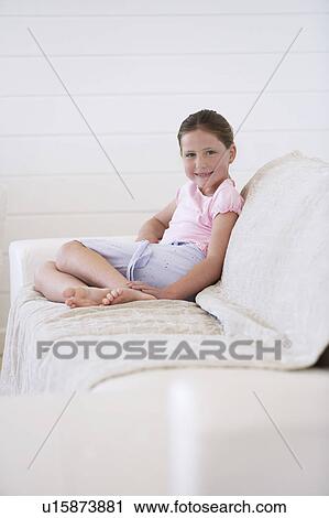 Stock Image - Girl sitting on sofa, full length, eye contact. Fotosearch