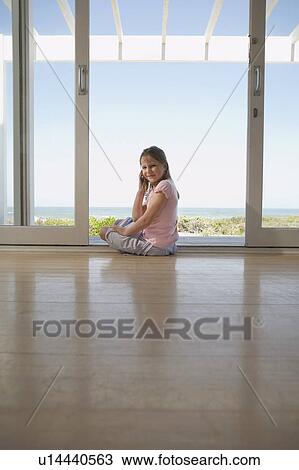 Stock Image - Girl using mobile phone, sitting on floor in doorway. Fotosearch