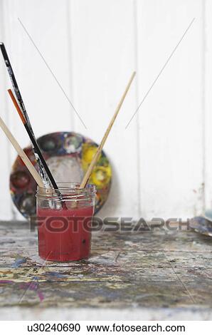 Stock Image - Glass with paintbrushes in artist's studio, close-up. Fotosearch