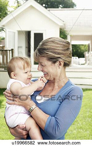 Stock Image - Grandmother and granddaughter in garden, half length. Fotosearch
