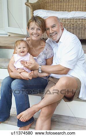 Stock Image - Grandparents sitting with granddaughter on porch. Fotosearch