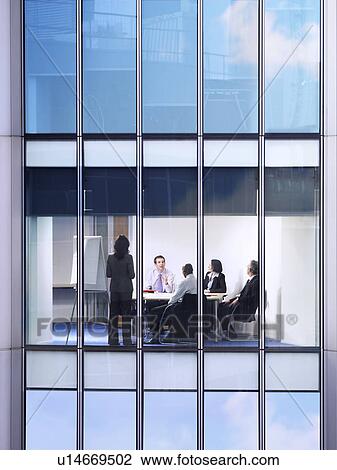 Stock Image - Group of business people at meeting in office, view from building exterior. Fotosearch