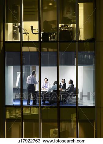 Stock Image - Group of business people at meeting in office, view from building exterior. Fotosearch