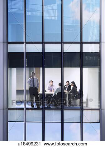 Stock Image - Group of business people at meeting in office, view from building exterior. Fotosearch
