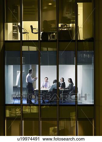 Stock Image - Group of business people at meeting in office, view from building exterior. Fotosearch