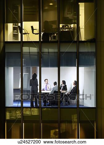 Stock Image - Group of business people at meeting in office, view from building exterior. Fotosearch
