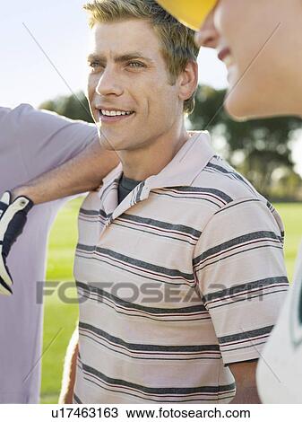 Stock Image - Group of young golfers on court, focus on smiling man. Fotosearch