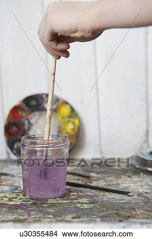 Picture - Hand rinsing paintbrush in jar of water. Fotosearch