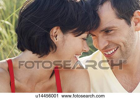 Stock Image - Happy Couple sitting face to face in grass, close up, portrait. Fotosearch