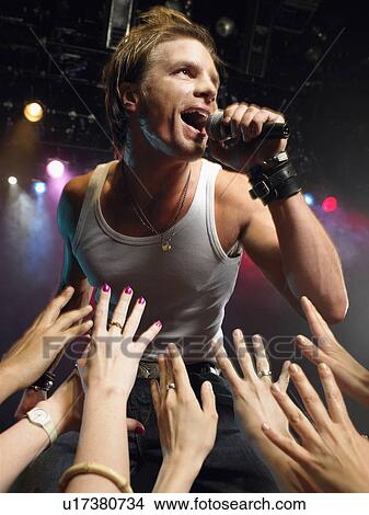 Picture - Low angle view of male rock star singing on stage with adoring fans reaching their hands up towards him. Fotosearch