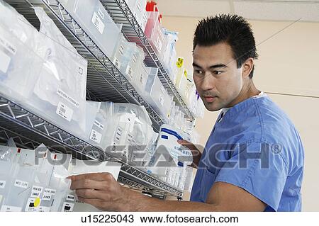 Stock Image - Male nurse standing by shelves with medical supply, low angle view. Fotosearch