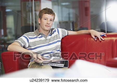 Male office worker sitting on sofa in office, portrait View Large Photo Image Stock Photo - Male office worker sitting on sofa in office, portrait. Fotosearch