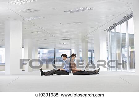 Stock Photography - Man and Woman Using Laptops in Empty Office Space. Fotosearch