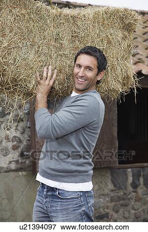 Stock Photo - Man carrying hay on shoulders, outdoors, portrait. Fotosearch