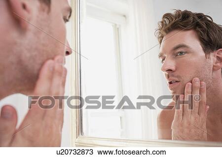 Stock Image - Man examining his stubble in mirror. Fotosearch