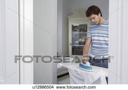 Picture - Man ironing shirt in living room. Fotosearch
