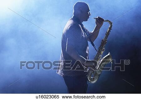 Stock Photography - Man Playing Saxophone in smoky place, side view. Fotosearch