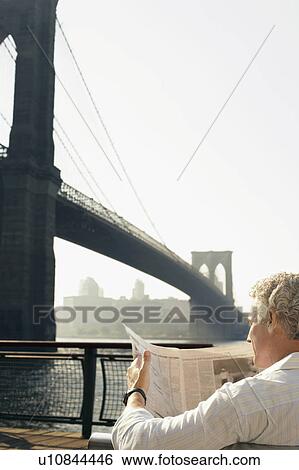 Stock Photograph - Man reading newspaper by Brooklyn Bridge. Fotosearch