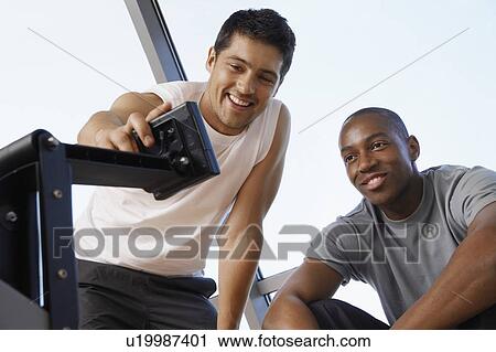 Stock Image - Man showing another man how to use control panel of exercise machine. Fotosearch