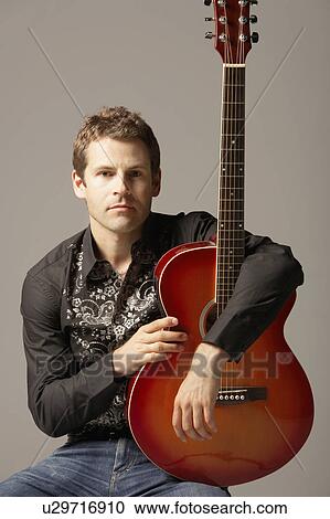Stock Image - Man sitting arms around Guitar, portrait. Fotosearch