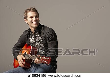 Stock Photograph - Man sitting, Playing Guitar, smiling. Fotosearch
