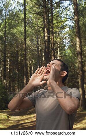 Stock Image - Man standing alone in woods yelling. Fotosearch