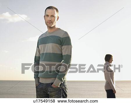 Man standing on beach with woman in background, portrait View Large Photo Image Stock Photo - Man standing on beach with woman in background, portrait. Fotosearch