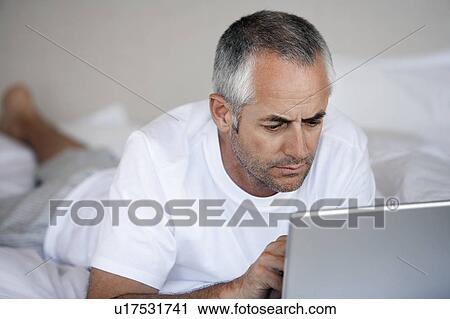 Man using laptop, lying on stomach on bed View Large Photo Image Stock Image - Man using laptop, lying on stomach on bed. Fotosearch