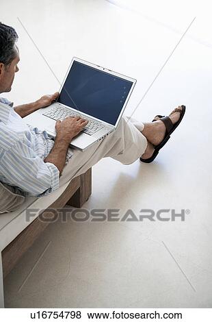 Man using laptop, sitting on sofa in living room, elevated view View Large Photo Image Stock Photo - Man using laptop, sitting on sofa in living room, elevated view. Fotosearch