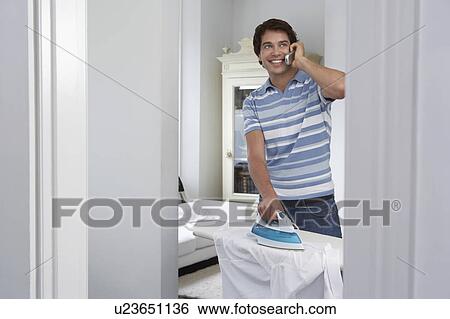 Man using mobile phone and ironing in living room View Large Photo Image Stock Photograph - Man using mobile phone and ironing in living room. Fotosearch