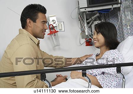 Stock Image - Man visiting woman in hospital. Fotosearch
