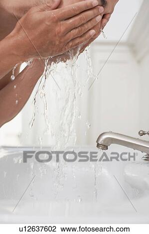 Stock Image - Man washing face in bathroom sink. Fotosearch