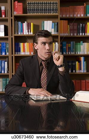 Man wearing suit chewing pen at desk in library View Large Photo Image Stock Image - Man wearing suit chewing pen at desk in library. Fotosearch