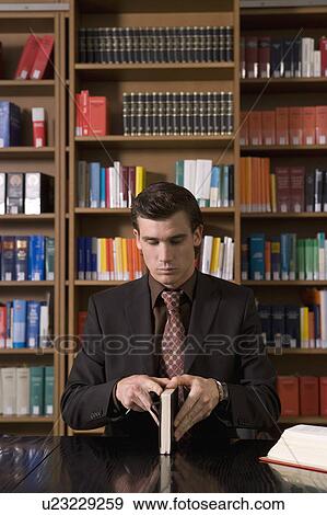 Stock Photo - Man wearing suit opening book at desk in library. Fotosearch