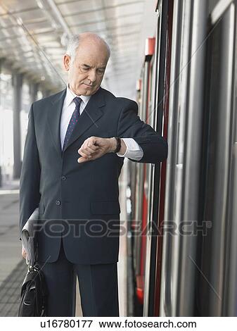 Stock Photo - Mature Businessman checking time, standing outside train in station. Fotosearch