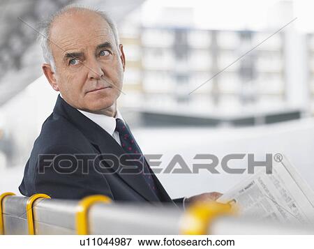 Mature Businessman Sitting on Bench with newspaper, looking over shoulder View Large Photo Image Stock Photo - Mature Businessman Sitting on Bench with newspaper, looking over shoulder. Fotosearch