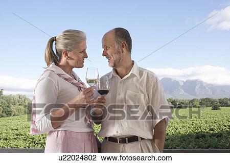 Stock Image - Mature couple holding wine glasses, toasting. Fotosearch