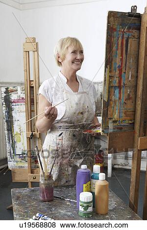 Stock Photo - Mature female artist painting at easel in art studiocanvas in studio. Fotosearch