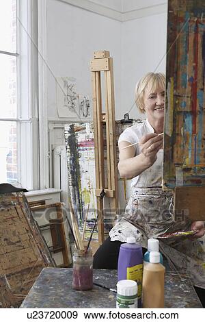 Mature female artist painting at easel in art studio View Large Photo Image Stock Photo - Mature female artist painting at easel in art studio. Fotosearch