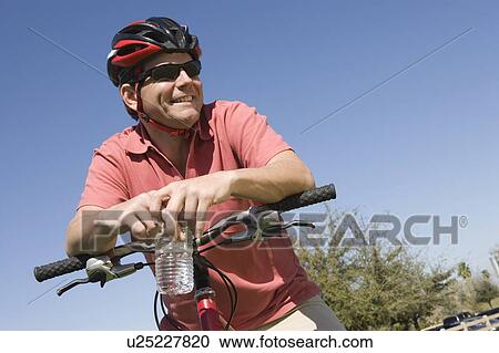Stock Image - Mature man in cycling helmet leans on bicycle handlebars. Fotosearch