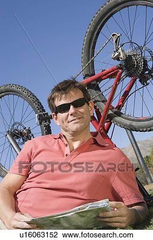 Stock Image - Mature man lies with ma, bike upside down. Fotosearch