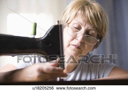 Stock Photograph - Mature woman adjusts foot of sewing machine. Fotosearch